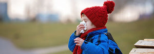 A little boy sitting on a bench wiping his nose with a tissue